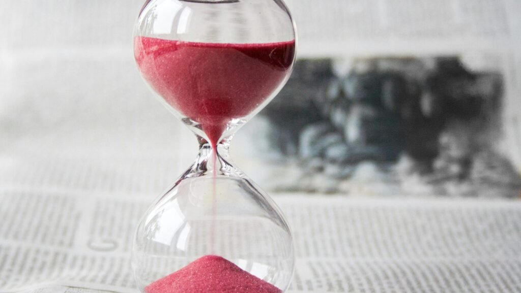 Close-up of a transparent hourglass with pink sand flowing, placed on a newspaper background.