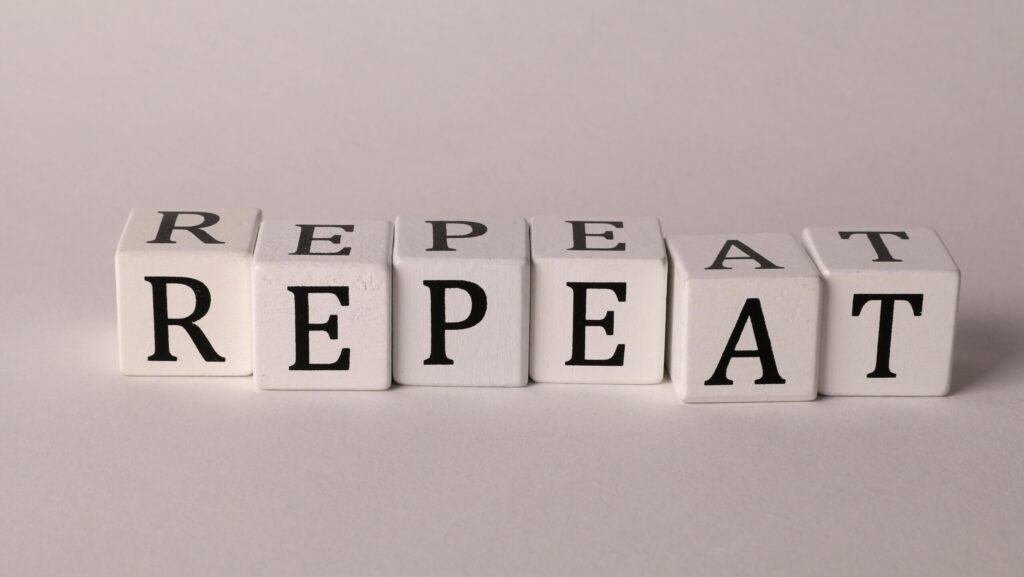 Wooden blocks arranged to spell 'REPEAT' on a neutral background.